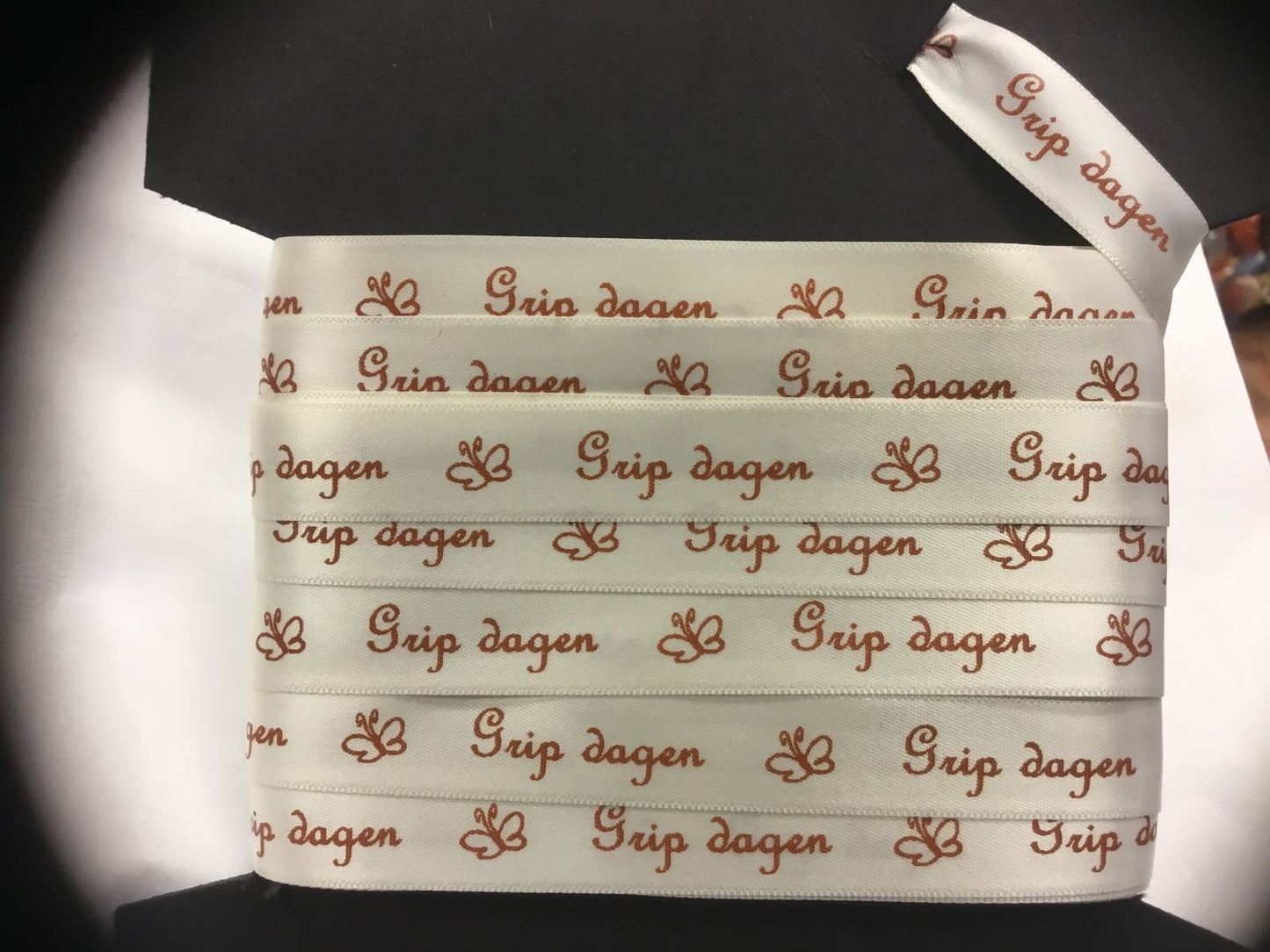 Bånd med tekst: «Grip dagen», kremhvitt med nøttebrun skrift. 15mm.