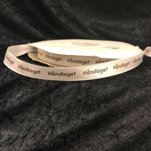 Bånd med tekst "Håndlaget", cremehvit m/brun skrift.  16 mm