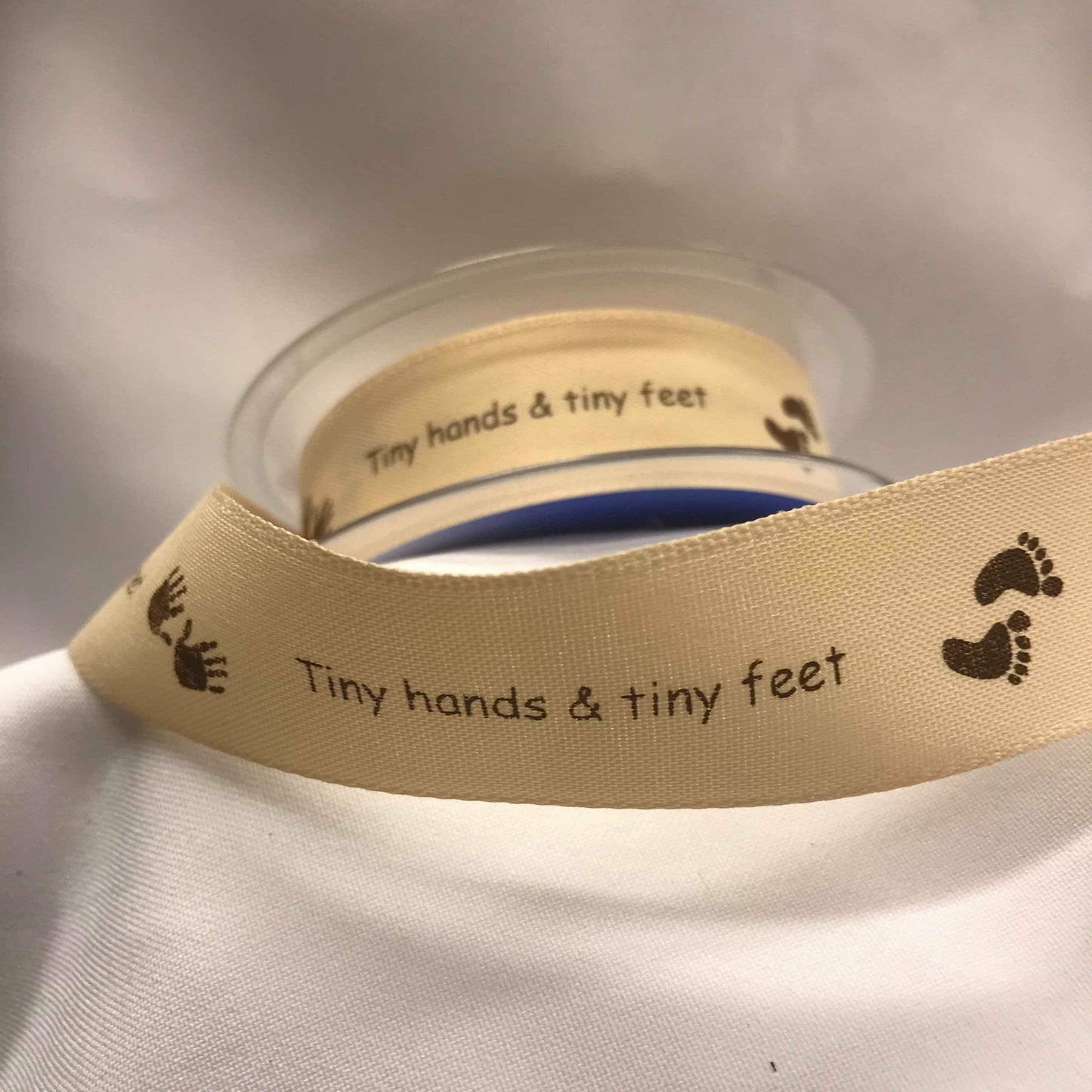 Bånd med tekst «Tiny hands & tiny feet», sandfarget m/brun skrift. 25mm.
