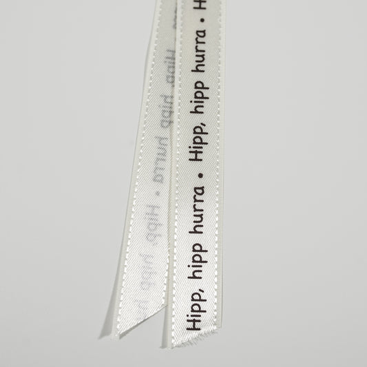 Bånd med tekst kremfarget med brun skrift " hipp hipp hurra ". 17mm
