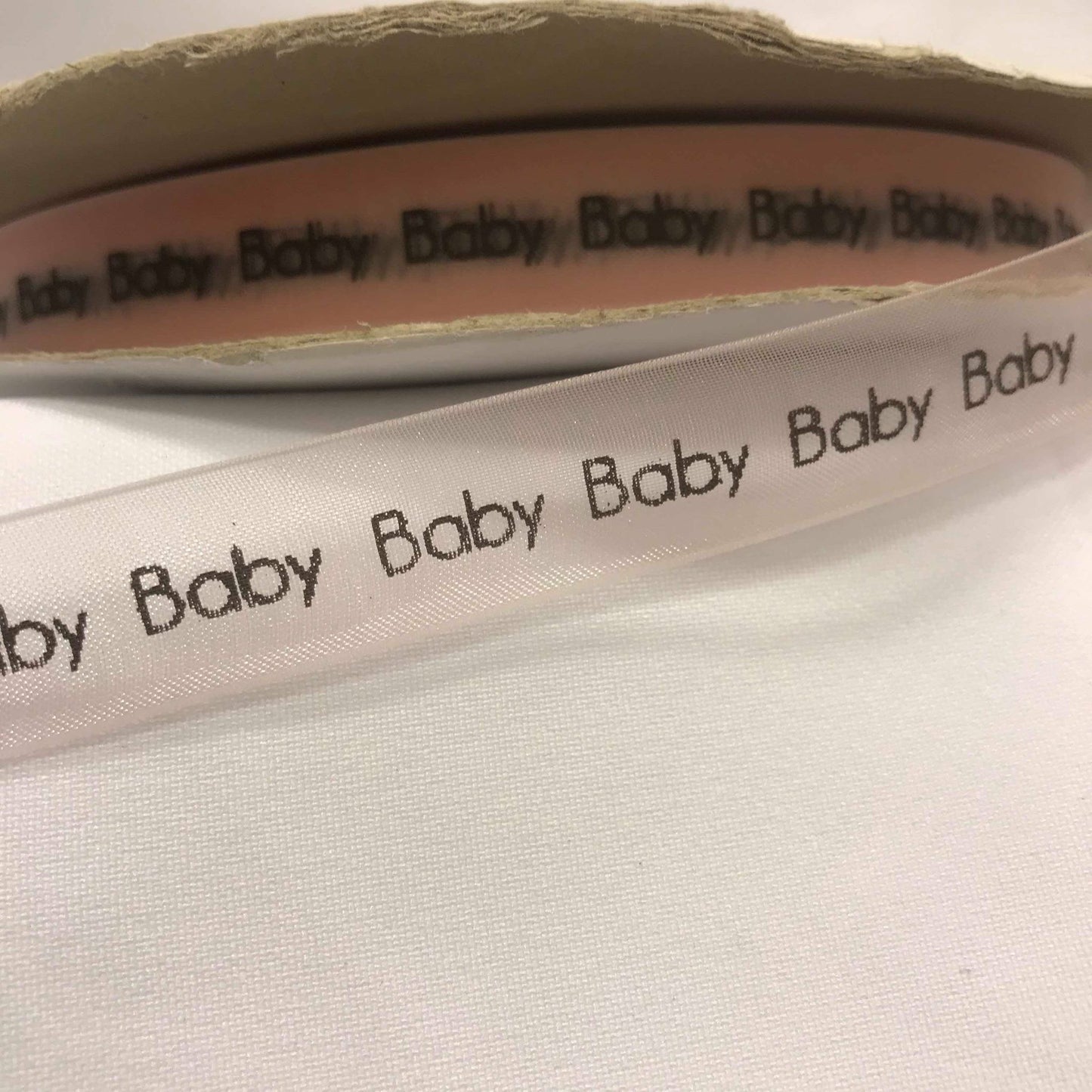 Bånd med tekst « Baby », lys rosa sheerbånd m/svart tekst. 16mm